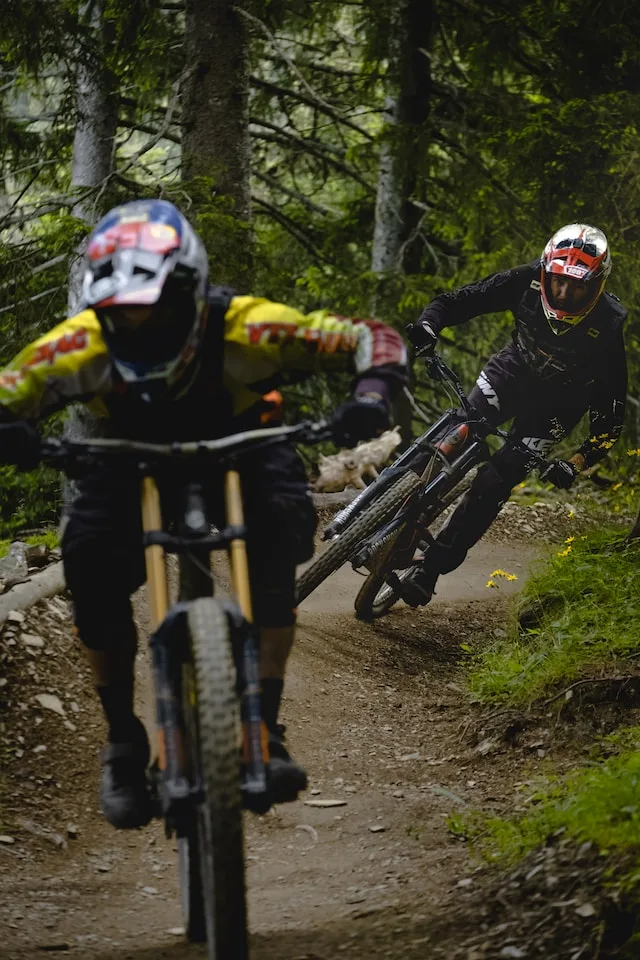 Two mountain bikers wearing helmets riding down an enduro track in the forest.