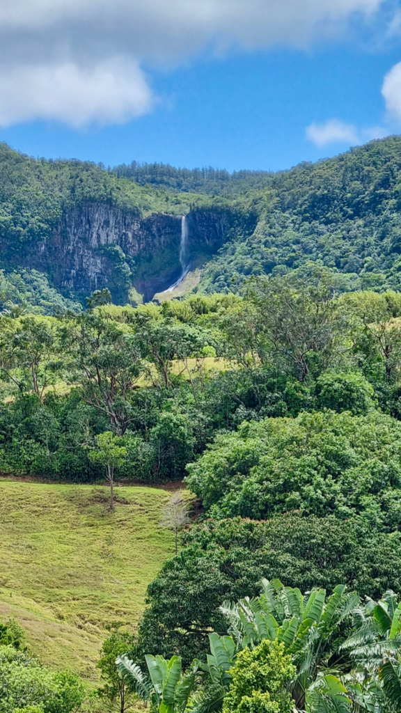 Waterfall in the middle of a wooded cliff with a blue sky