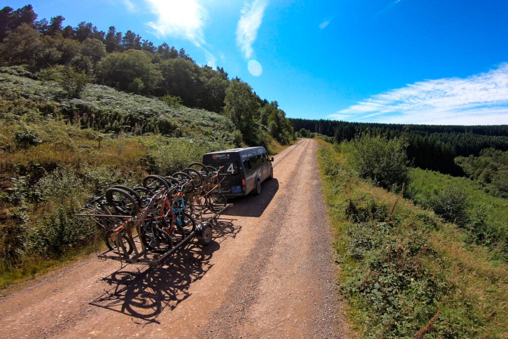 A van parked beside a dirt road, featuring bicycles mounted on its side.