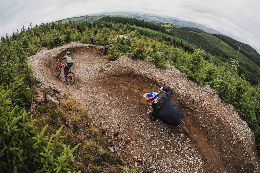 A group of cyclists riding bikes along a mountain trail, surrounded by lush greenery and rocky terrain.