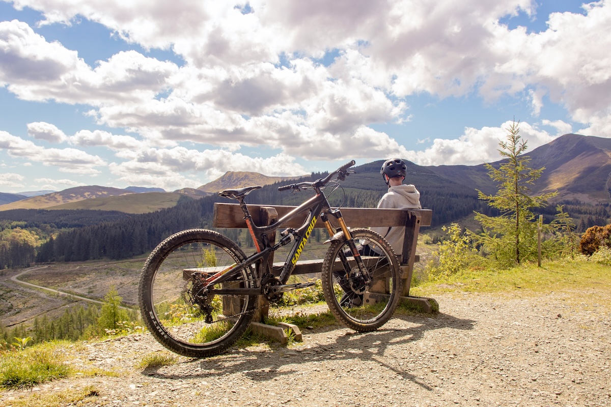 A man sits on a bench with a bicycle resting against it, enjoying a moment of relaxation outdoors.