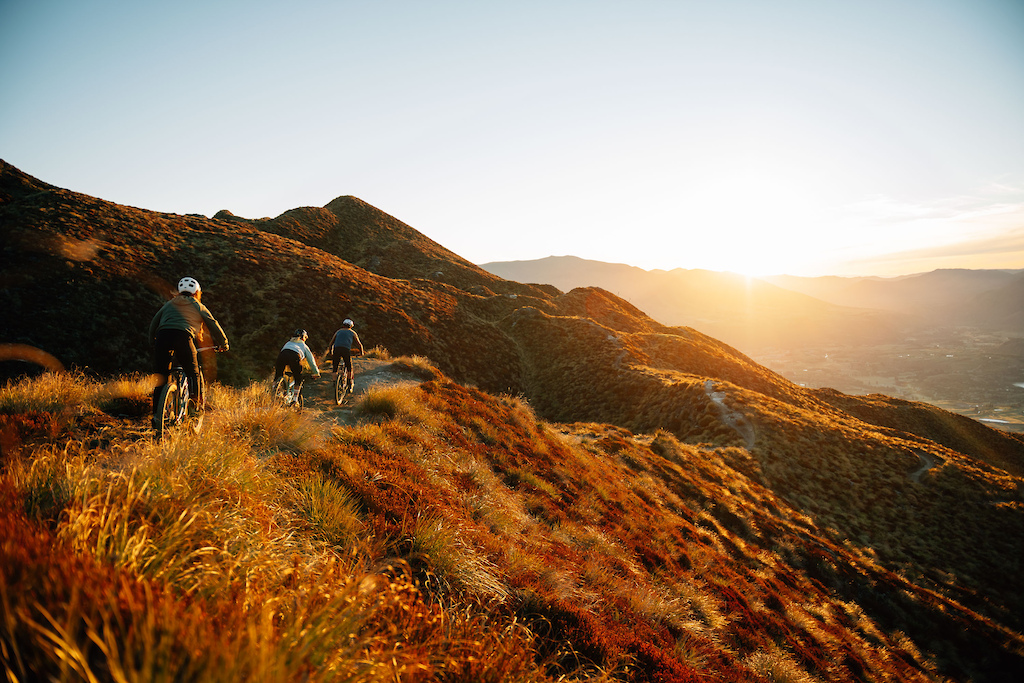 A group of cyclists riding bikes along a mountain trail, surrounded by lush greenery and rocky terrain.